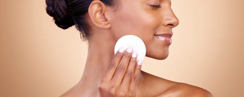 Woman, cotton pad and skincare of face cosmetics for aesthetic wellness on studio background. Happy indian female model, clean beauty and facial dermatology product for makeup removal, shine and glow.